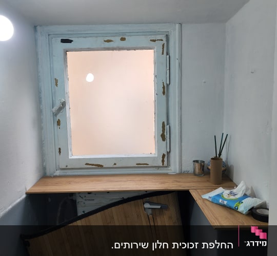 חלון עץ עם זכוכית חלבית מעל משטח בחדר שירותים